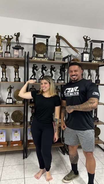 Rafael Calil e uma aluna diante da estante de troféus da Dr. Fitness